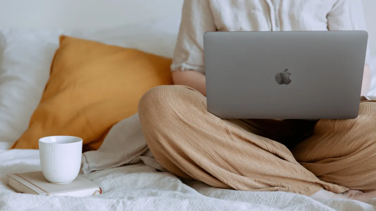 photo of person sitting on top of a bed with a laptop and a coffee cup