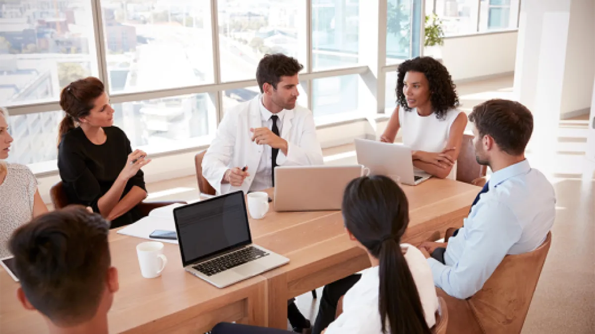 5 people sitting around a conference table with laptops in discussion