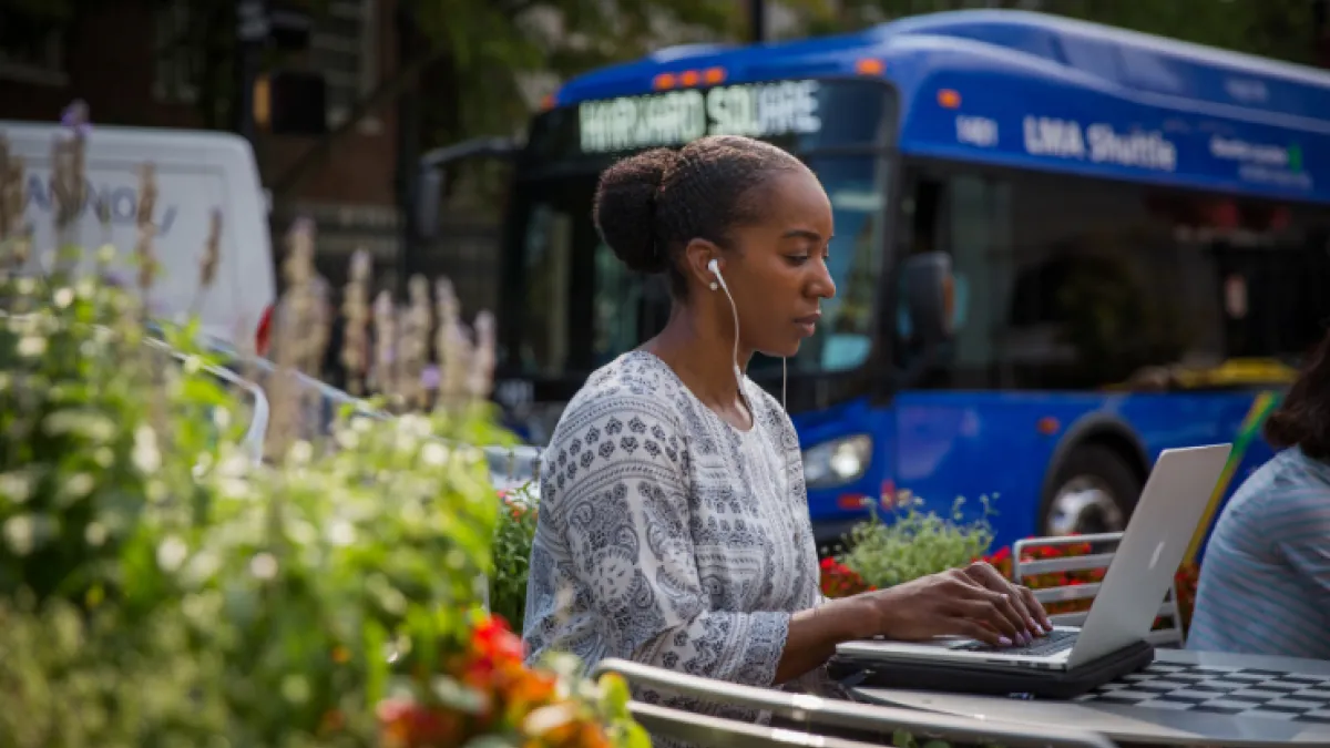Photo of woman on laptop sitting at a picnic table outside in the summer