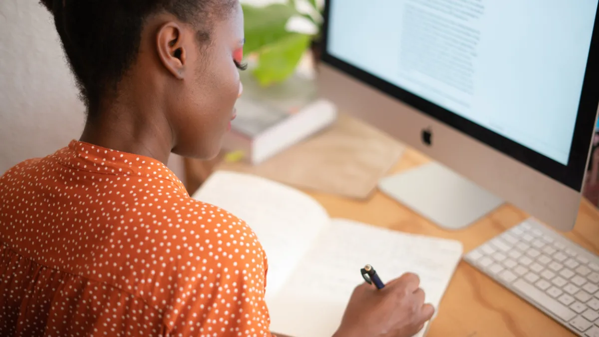 Image of woman wearing orange top writing in a journal with a pen.