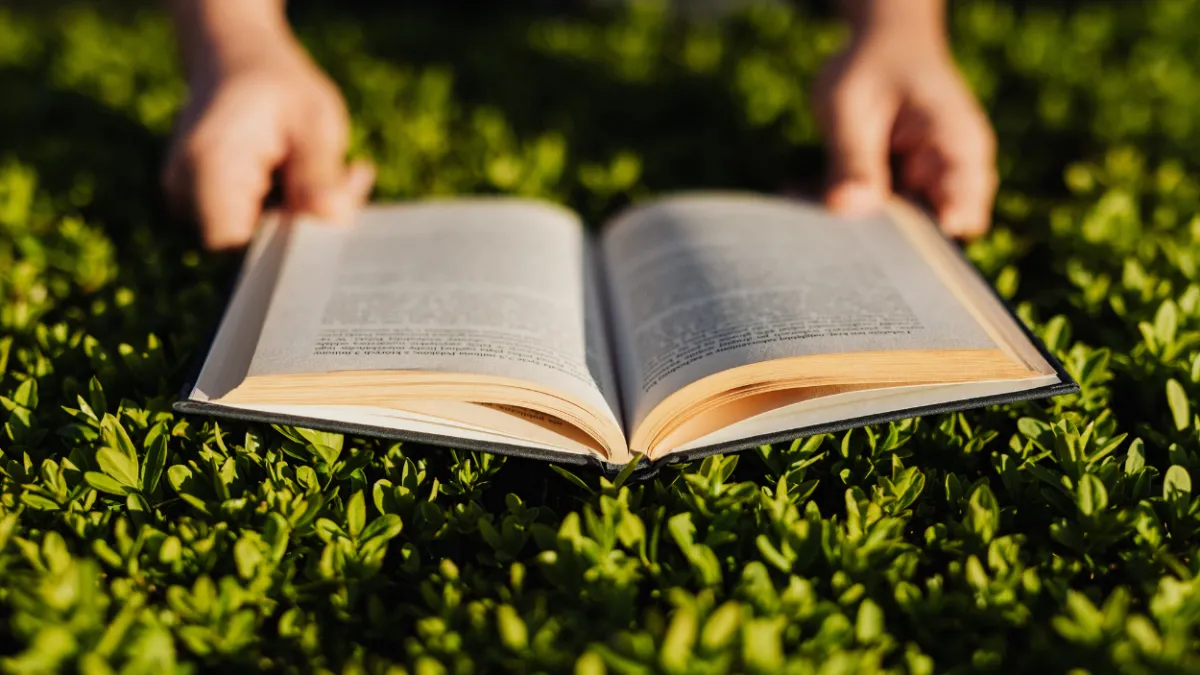 Photo of a person's hands holding a book open in the grass