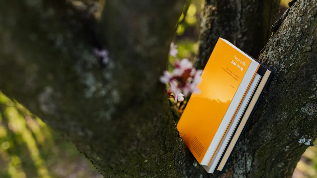 A stack of books sits on a tree branch with spring cherry blossoms blooming in the background.