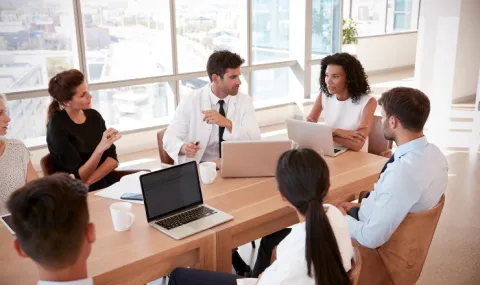 Image of group of professionals sitting around a wooden meeting table discussing a topic