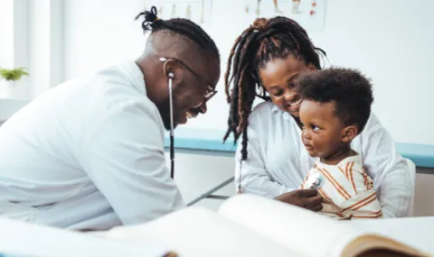 Photo of pediatrician treating young child who is sitting on mother's lap