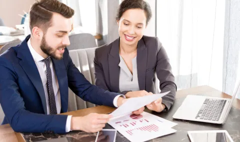 Image of woman and man in professional attire sitting at a wooden table discussing data graphics