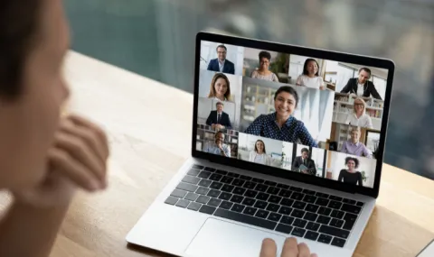 Image of a laptop that is presenting an online meeting as a woman looks on