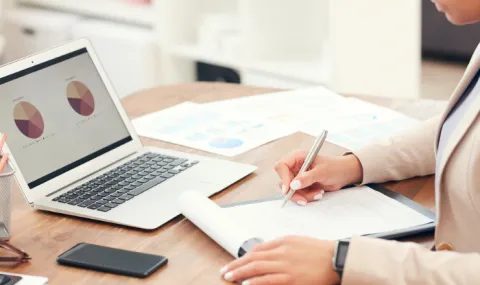 Photo of woman writing at desk with laptop and notepad