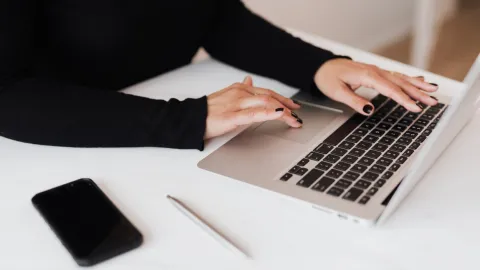 Photo of laptop with woman's hands hovering over keyboard on white desk surface