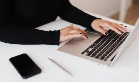 Photo of laptop on white desk surface with woman's hands hovering over keyboard