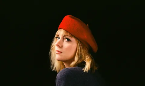 Photo of Saskia Keultjes, a woman with blond hair wearing a red beret looking back over her shoulder against a black backdrop