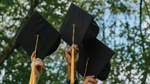 Photo of three people holding graduation caps against a background of trees
