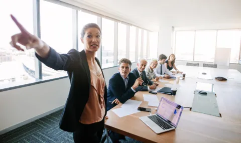 Professional woman pointing at board in team meeting.